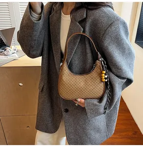 Detail of brown checkered woven handbag with beaded charm and leather strap worn by model