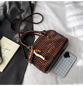 Detalle del bolso de mano plisado marrón café con colgante de cuentas y correa