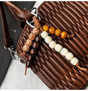 Detalle del bolso de cuero marrón oscuro con pliegues ondulados y colgante de madera retro