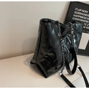 Detail view of the quilted glossy leather texture and silver chain strap on the black tote bag