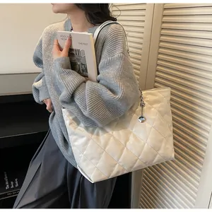 Detail of white quilted tote bag with metallic pendant and smooth leather texture finish