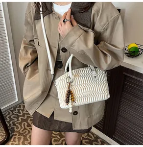 Detalle de bolso blanco plisado con colgante de cuentas de madera y herrajes plateados