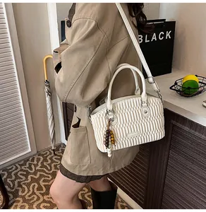 Detalle del bolso de mano plisado blanco roto con colgante de madera y correa de hombro ajustable