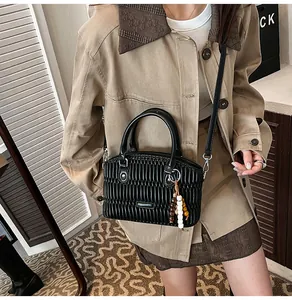 Detalle de bolso negro plisado con correa ajustable y colgante con cuentas de madera