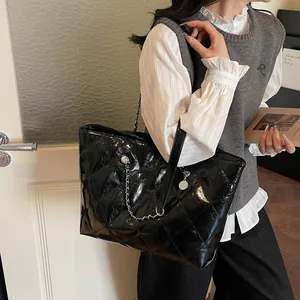 Glossy black quilted tote bag with silver chain strap shown on model's shoulder