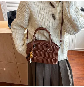 Vista detallada del bolso de mano marrón acolchado con colgante de cuentas de madera