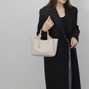 Grand sac cabas beige en cuir grainé avec pendentif argenté porté par un mannequin