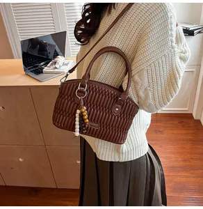 Primer plano del bolso de cuero marrón con diseño plisado y detalle de colgante de cuentas