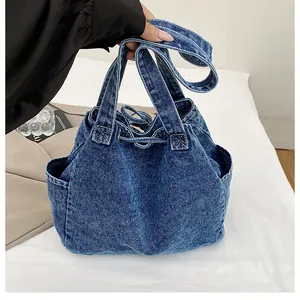 Detalle de bolso tote de mezclilla azul oscuro con cierre de cordón y asas dobles
