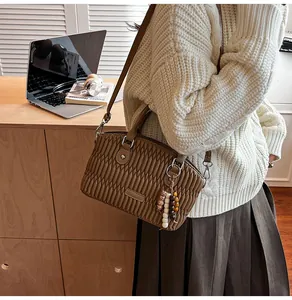 Detalle de bolso matelassé marrón café con colgante de cuentas y asas de cuero