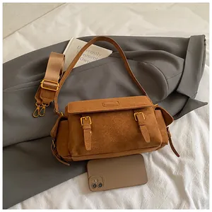 Close-up of brown suede messenger bag with dual straps and polished metal buckles