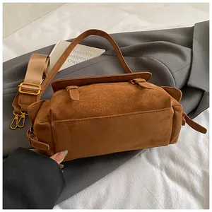 Close-up of caramel brown matte suede messenger bag with gold buckles and wide strap