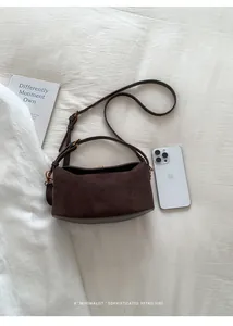 Détail du sac bandoulière en daim marron foncé avec boucles métalliques et fini mat