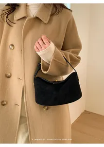 Détail d'un sac hobo rétro en daim noir avec boucle dorée sur un manteau en laine