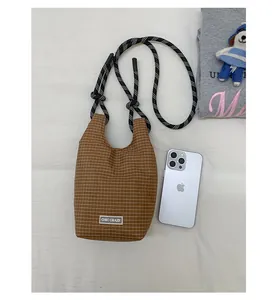 Detailaufnahme der braun karierten Canvas-Umhängetasche mit dickem Seilgurt und Markenlabel