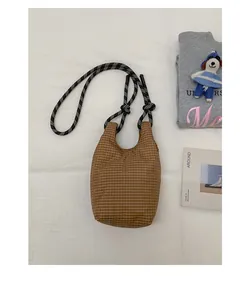Detail einer braun karierten Beuteltasche mit schwarz-weiß gewebten Kordelträgern