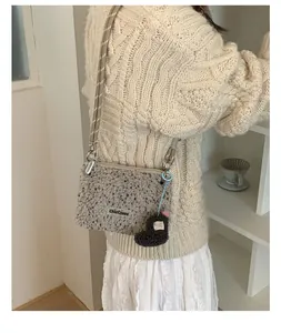 Détail du sac bandoulière en peluche avec sangle rayée et breloque botte sur un mannequin