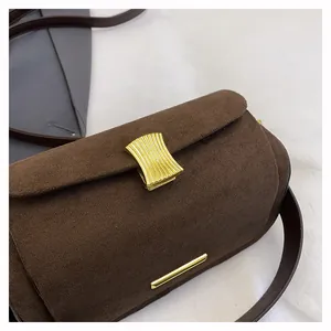 Dettaglio del tessuto in pelle scamosciata opaca e fibbia dorata su borsa marrone