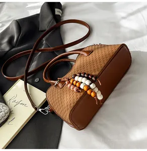 Detail of a brown textured crossbody bag featuring woven panels and wooden bead tassel decor