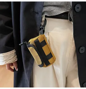 Detailed view of mini yellow canvas cylinder bag hooked on trousers for lipstick or earphones