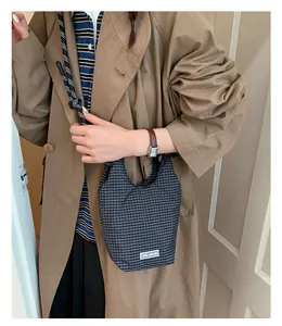 Detail der karierten Beuteltasche mit Seilgriff und Chic Craze Label auf braunem Mantel