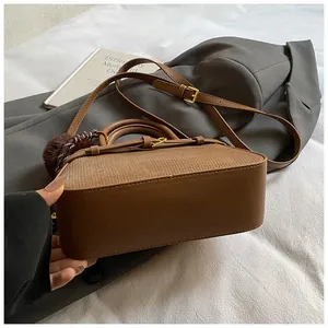 Detail of a brown bucket bag with mixed textures, plush pompom, and shoulder strap on a bed