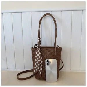 Détail d'un sac seau tressé marron foncé avec bandoulière et foulard en soie à pois