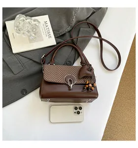 Detail of a brown leather handbag with metallic clasp, beaded charm, and Matisse book