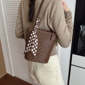 Sac seau marron à texture tressée avec foulard à pois porté par un mannequin en intérieur