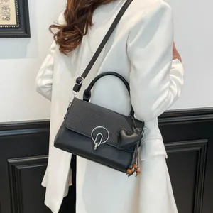 Chic black crossbody bag with V-shaped texture and heart charm on white blazer outfit