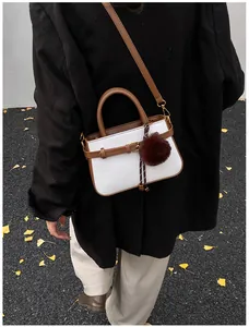 Detail of white woven texture bucket bag with brown strap and plush ball on autumn leaves