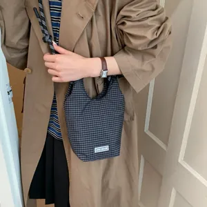 Schicke schwarz-weiß karierte Beuteltasche mit geflochtenem Riemen am Trenchcoat-Model