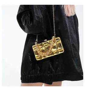 On-body shot of gold acrylic evening bag with beaded handle and metal chain on black leather