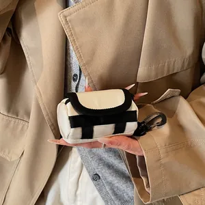 Mini canvas lipstick and earphone bag with black strap held by a person in a trench coat