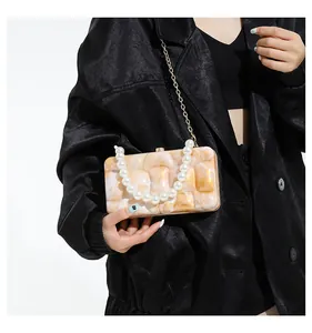 Detail of amber marble acrylic bag with pearl handle and gold chain strap on black outfit
