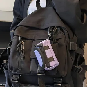 Mini purple nylon backpack charm and headphone case hanging on a black travel bag