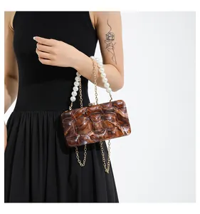 Detail of acrylic handbag with marble texture, pearl handle, and gold metal chain strap