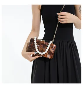 Detail of amber marble acrylic clutch with large pearl handle and golden chain strap