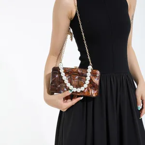 Brown marble acrylic evening clutch with pearl handle and gold chain on model