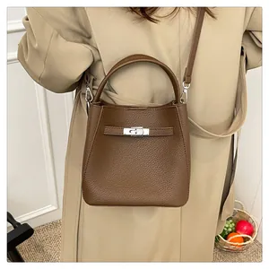 Detail shot of brown lychee grain leather bucket bag with silver lock on tan trench coat
