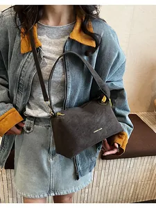 Dettaglio della borsa a tracolla in pelle scamosciata marrone con logo dorato sul modello