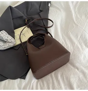 Close-up of deep brown lychee grain leather bucket bag with top handle on white linen