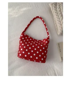 Detailed close-up of a red and white polka dot canvas shoulder bag on textured fabric