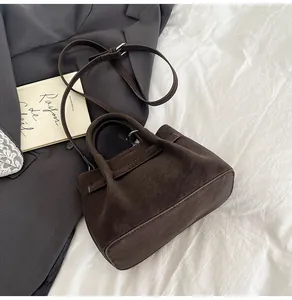 Detail of dark brown suede bucket bag featuring double handles and adjustable strap