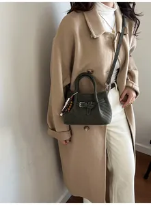 Detail of dark green suede handbag with leather buckle and bead charm on an oat coat