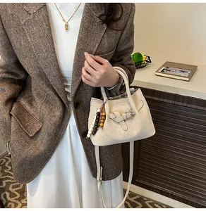 Detail of cream V-quilted handbag with beaded charm and adjustable strap held by a model