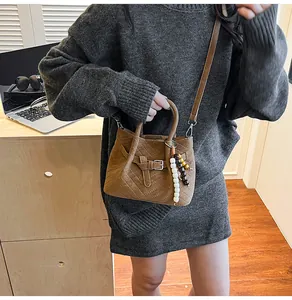 Detail of brown V-quilted faux suede handbag with beaded charm on side in stylish setting