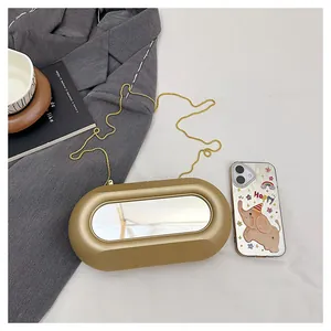Détail du sac capsule doré avec miroir ovale intégré et fine bandoulière en chaîne dorée