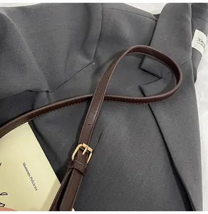 Close-up of brown suede bucket bag shoulder strap with gold buckle and stitching