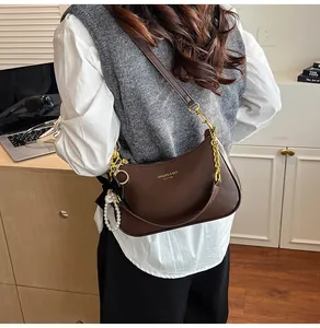 Dettaglio borsa in pelle marrone con logo dorato e ciondolo con perle e fiocco nero